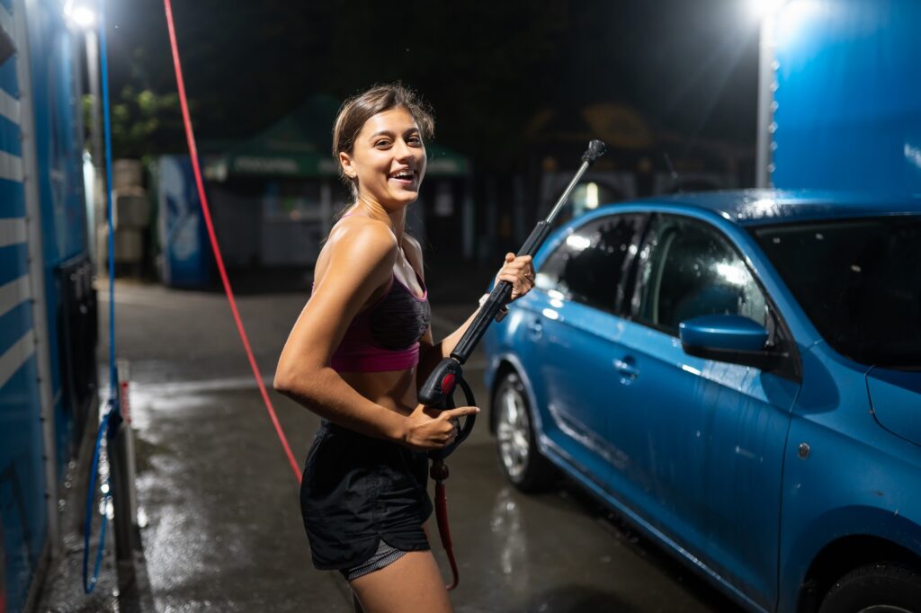 Young woman washing blue car at car wash